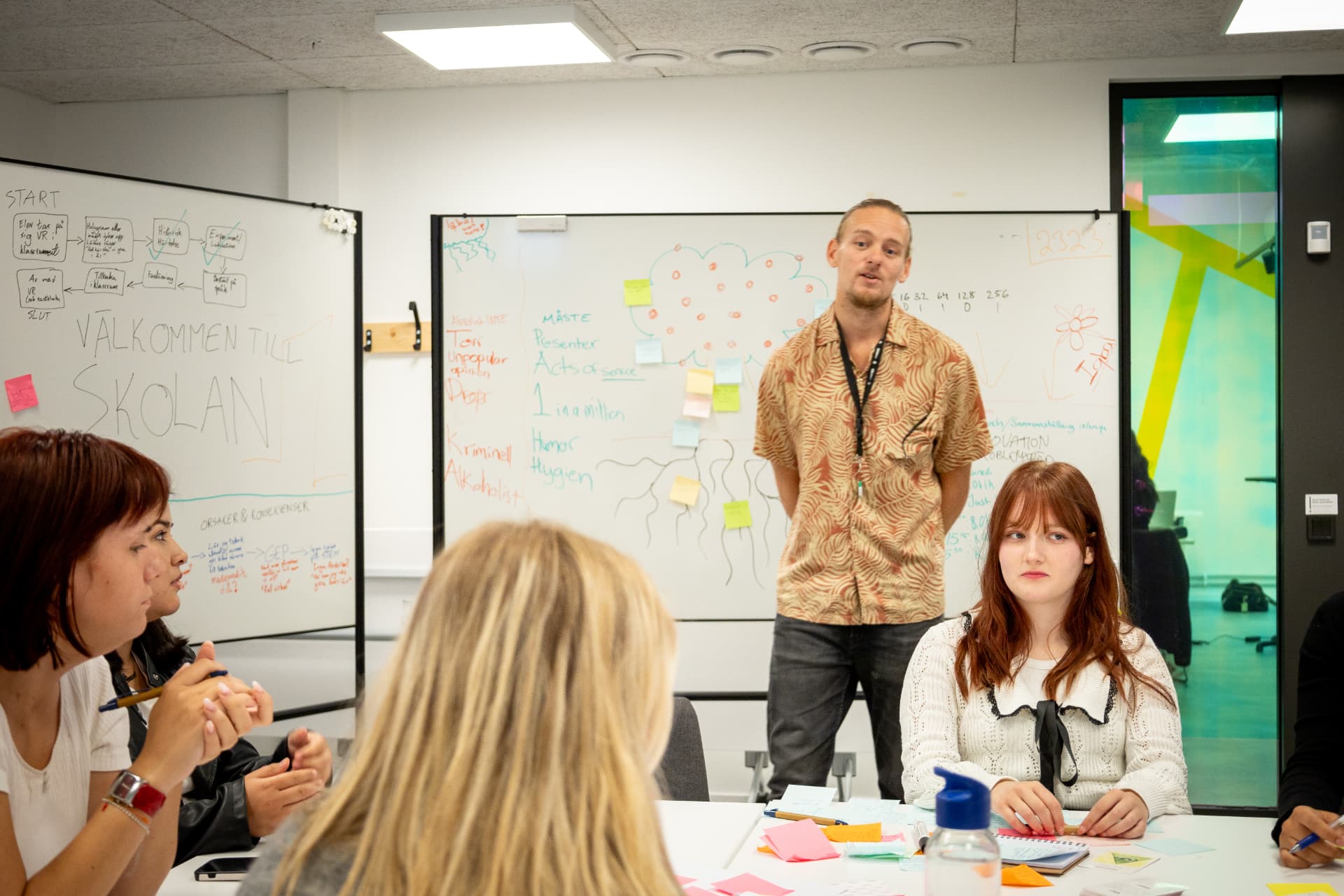 Deltagare samtalar under en workshop framför whiteboardtavlor med skisser och färgglada lappar.